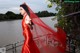 A woman in a red dress standing by a body of water.