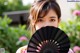 A woman holding a black fan in front of her face.