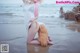 A woman kneeling on the beach with a dog.