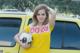 A young woman holding a soccer ball in front of a yellow van.